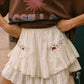 Person wearing a brown sweatshirt with pink graphics and a white embroidered skirt.