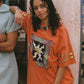 Woman wearing an orange graphic t-shirt with a cat design, standing next to a person in a light blue shirt.