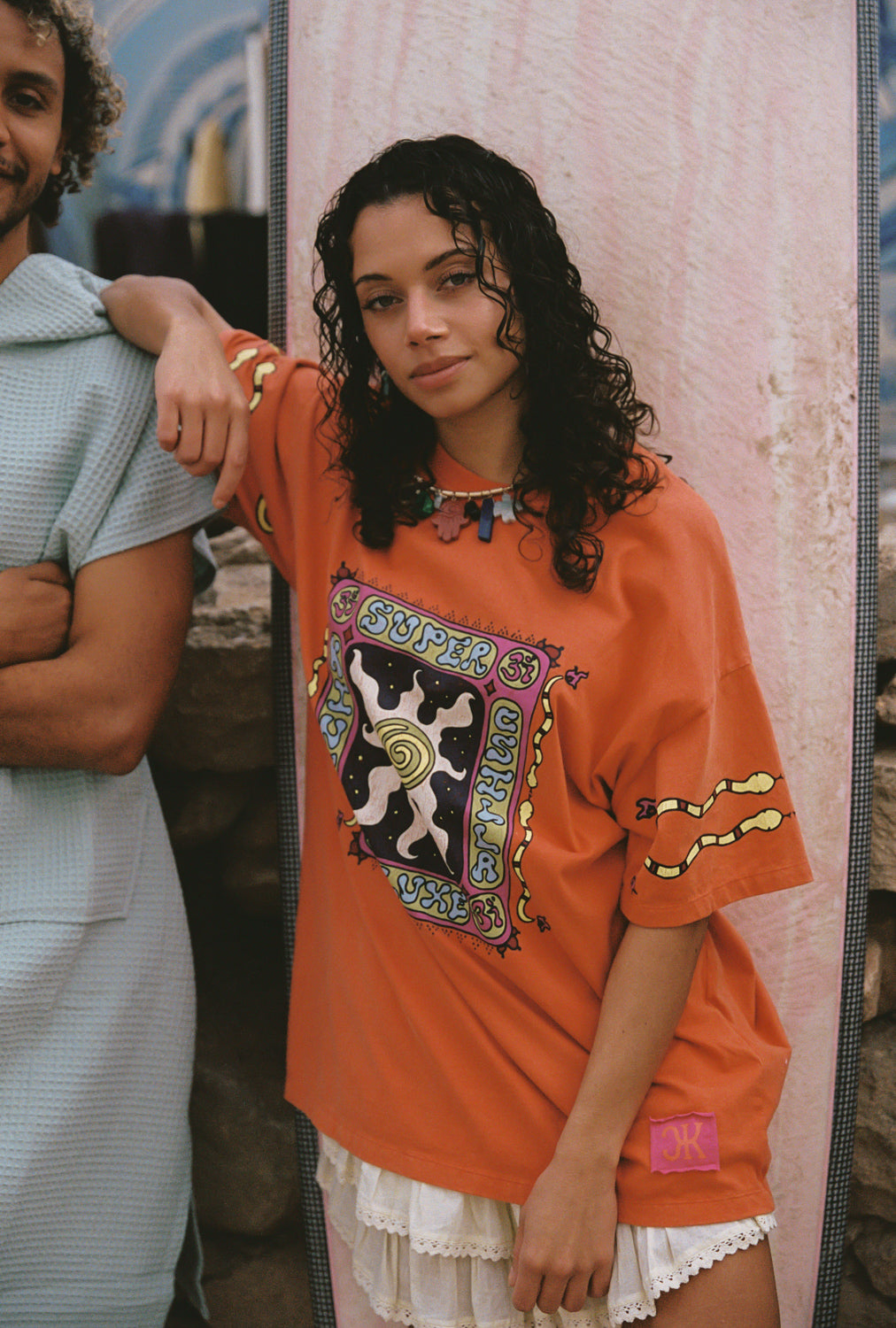 Woman wearing an orange graphic t-shirt with a cat design, standing next to a person in a light blue shirt.