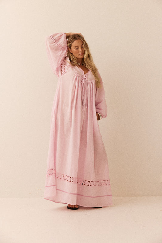 Woman wearing a pink long dress with lace details on a beige background