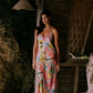 Woman in a colorful dress standing in front of a rustic wooden structure.