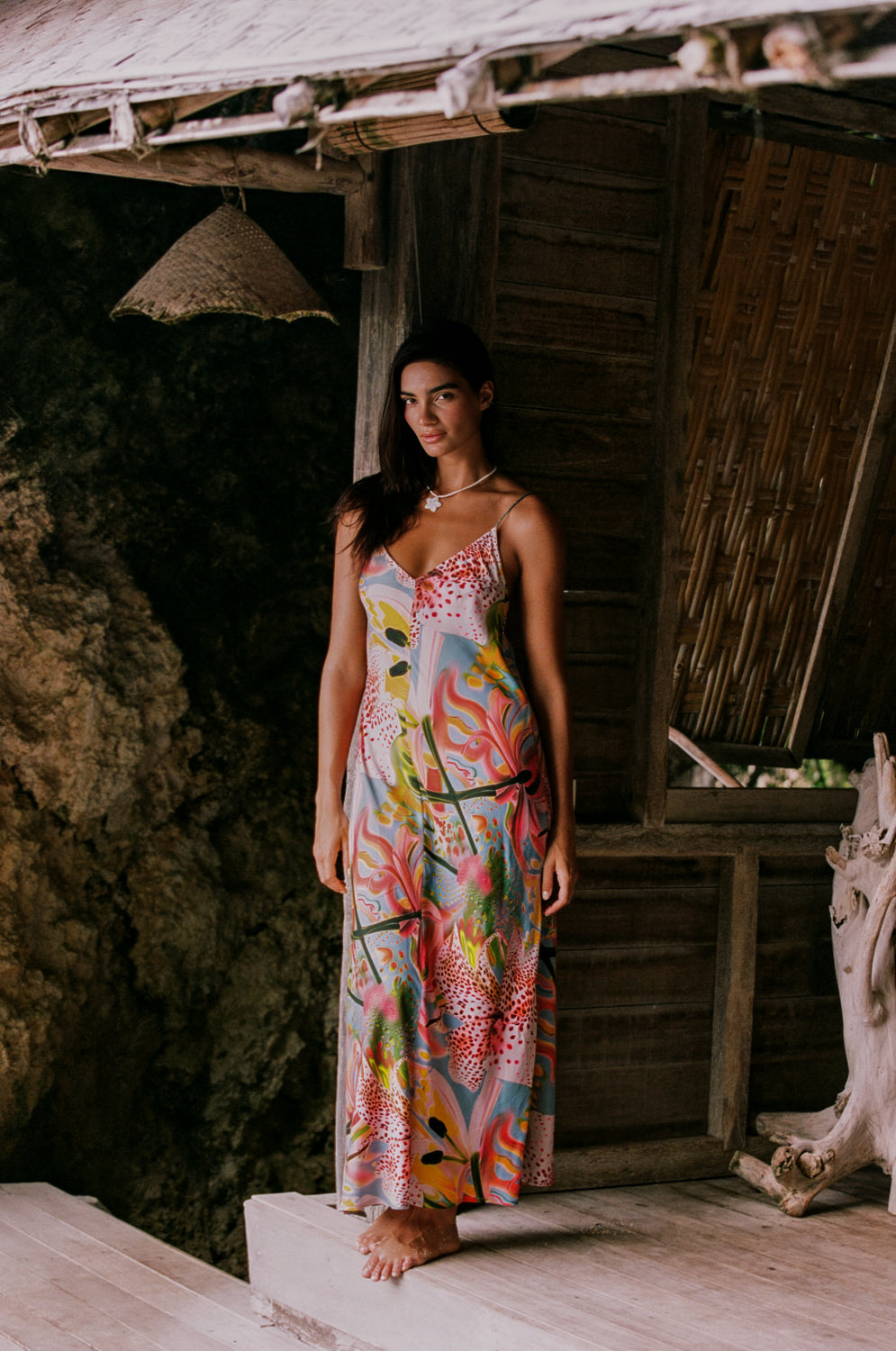 Woman in a colorful dress standing in front of a rustic wooden structure.