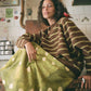 Woman wearing a brown and green striped sweater with a green polka dot bag in a kitchen.