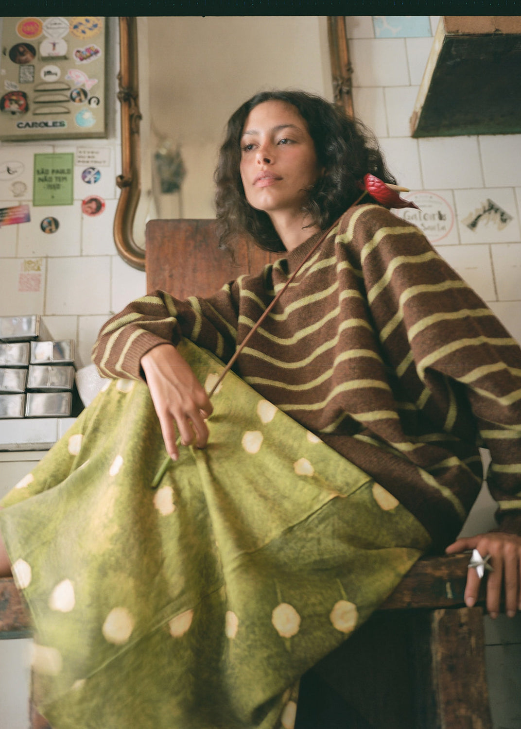 Woman wearing a brown and green striped sweater with a green polka dot bag in a kitchen.
