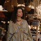 Woman in a patterned dress standing in a market with wicker baskets and decor.