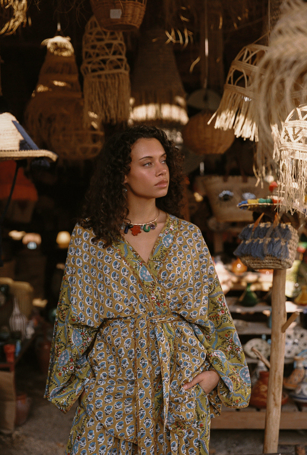 Woman in a patterned dress standing in a market with wicker baskets and decor.