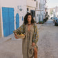 Woman in a patterned dress holding a basket in a narrow street with white walls and blue doors.