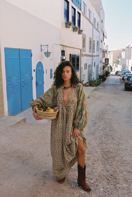 Woman in a patterned dress holding a basket in a narrow street with white walls and blue doors.