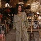 Woman in a patterned dress standing in a market with various wares hanging above her.