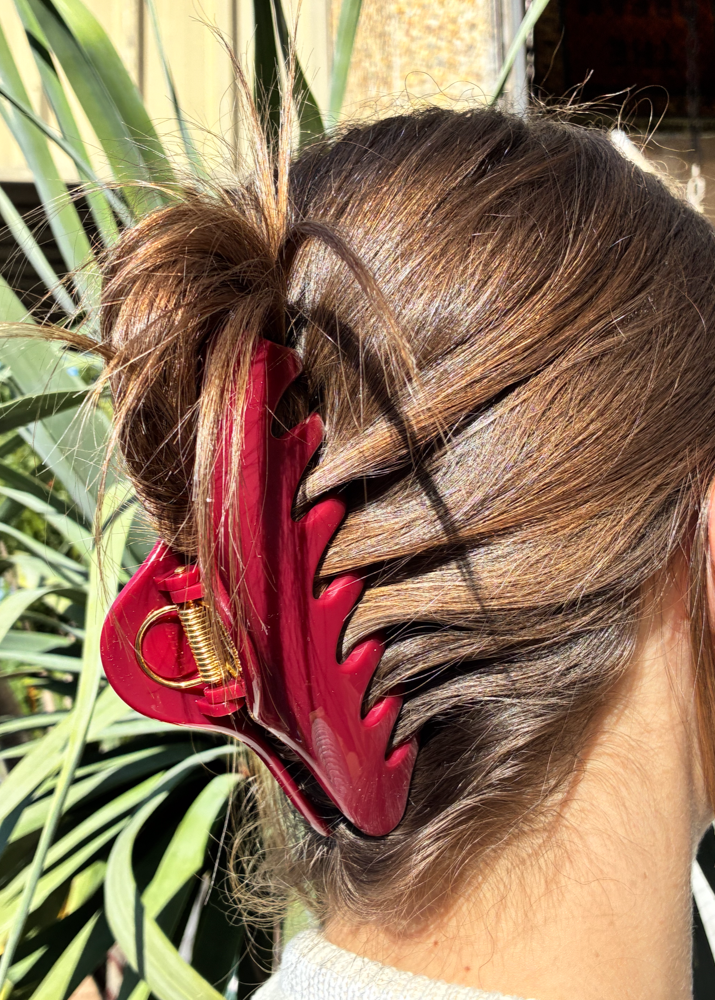 Close-up of a person's hair with a red claw clip against a blurred natural background