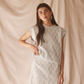 Woman wearing a patterned light blue set against a beige curtain background