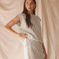 Woman wearing a light blue patterned set against a beige curtain background