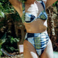 Woman wearing a blue and green patterned bikini set outdoors with greenery in the background