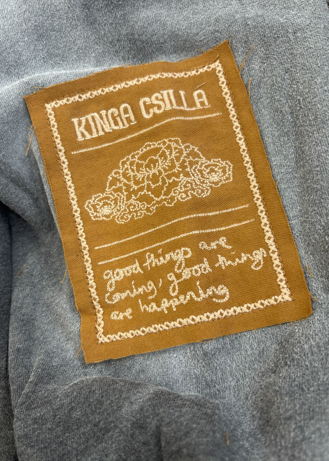 Brown patch with embroidered text and design on a gray fabric background