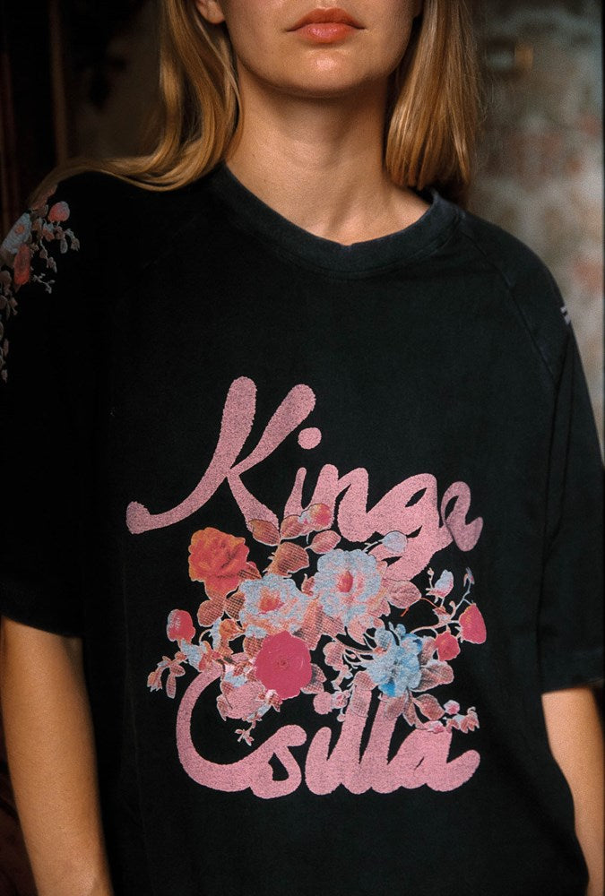 A close-up of a model wearing a black oversized t-shirt with a pink 'Kinga Csilla' graphic and a colorful floral print in pink, red, and blue.
