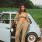 Woman standing next to a vintage car in a a khaki lace bralette and flare pant
