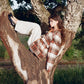 Person sitting in a tree wearing a plaid shirt and white pants.
