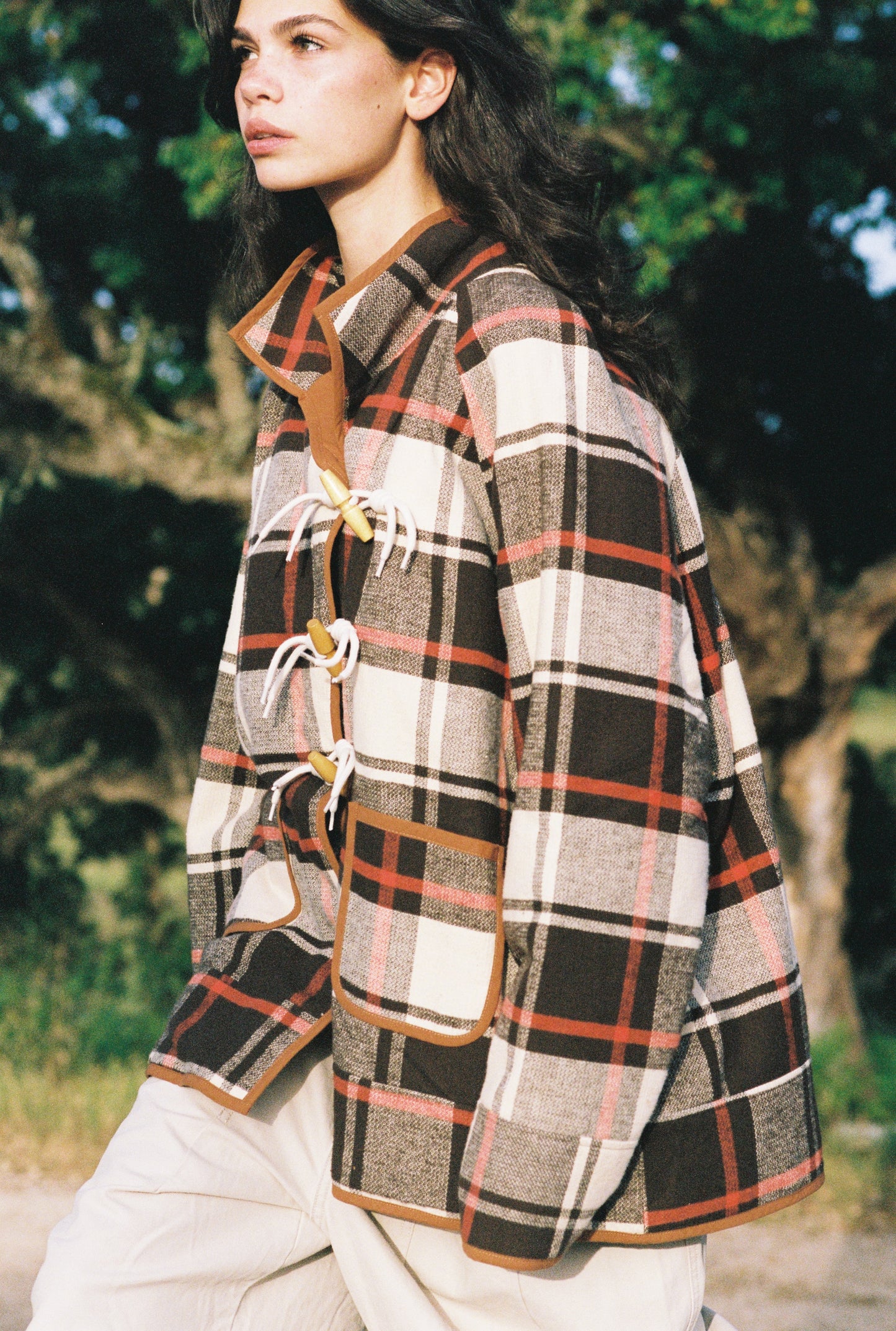 Woman wearing a plaid coat outdoors with trees in the background