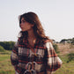 Woman wrapped in a plaid blanket standing in a field with trees in the background