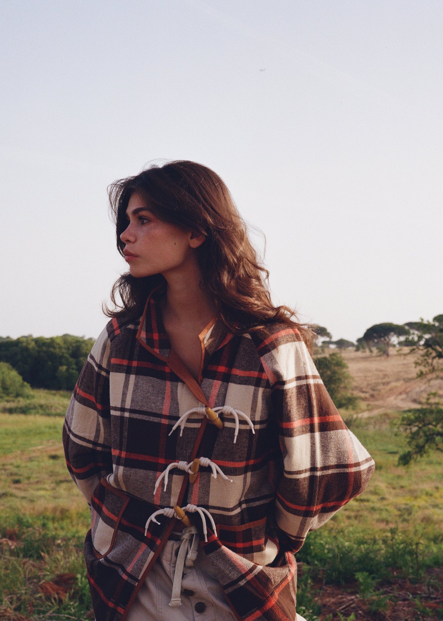 Woman wrapped in a plaid blanket standing in a field with trees in the background