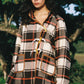 Woman wearing a plaid jacket outdoors with trees in the background