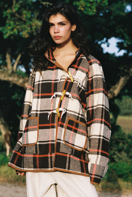 Woman wearing a plaid jacket outdoors with trees in the background