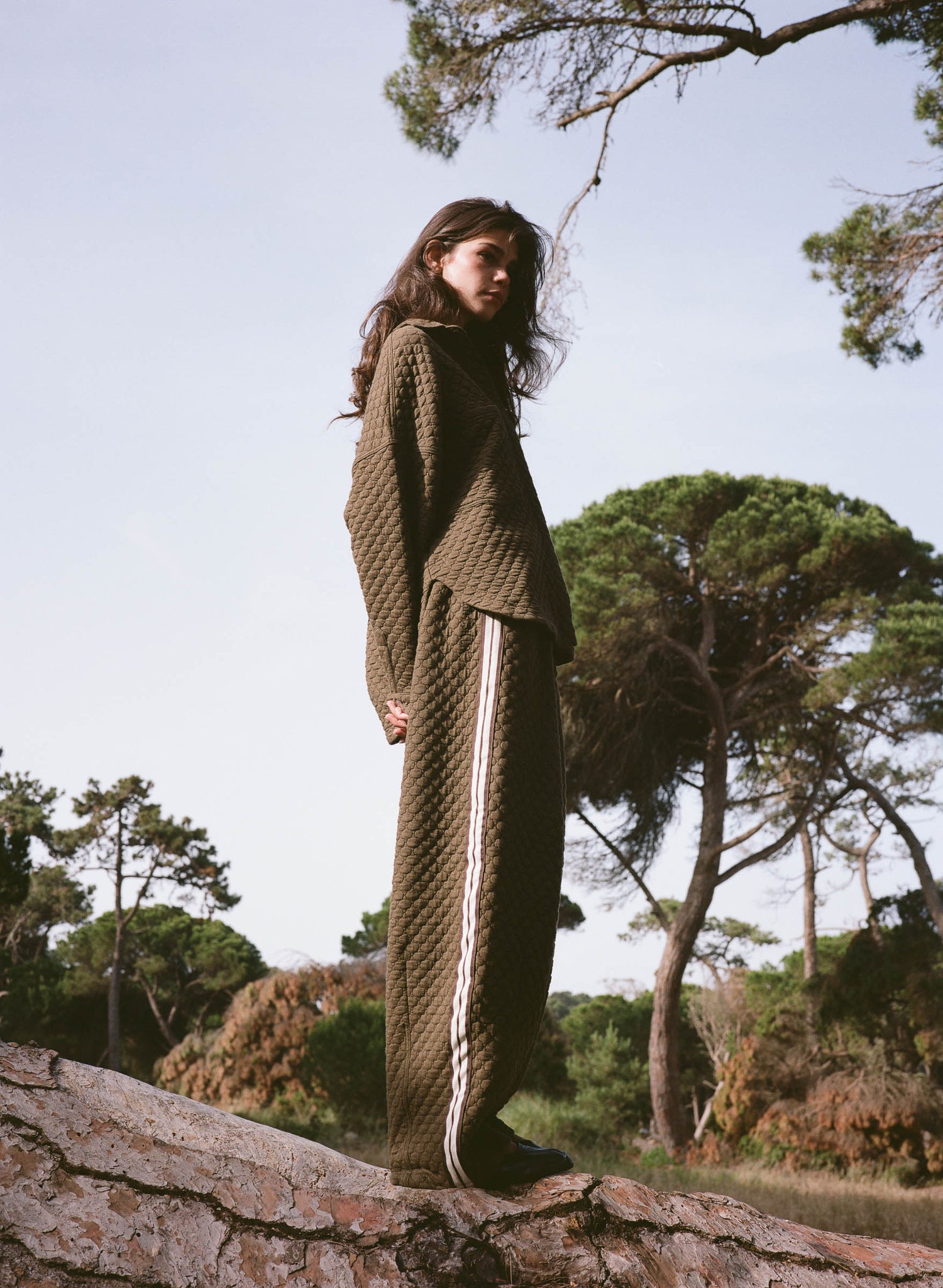 Person wearing a green textured outfit standing on a log with trees in the background