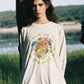 Woman wearing a long-sleeve shirt with a colorful graphic design outdoors by a lake.