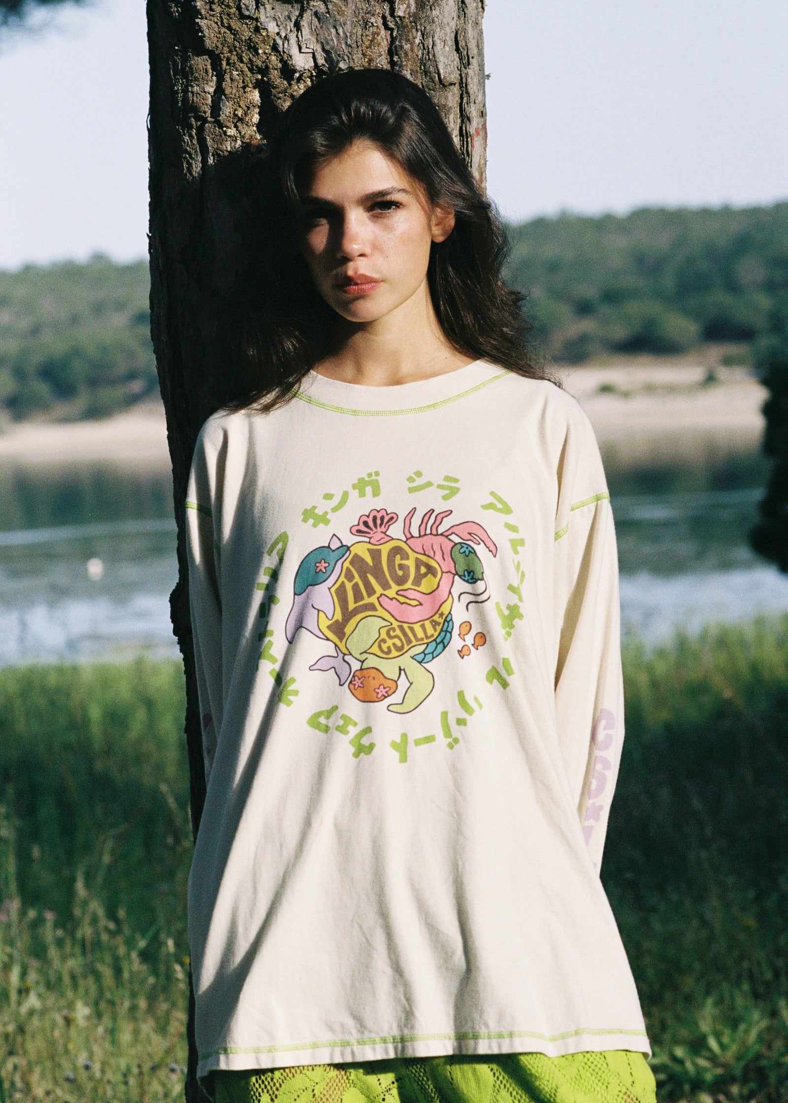 Woman wearing a long-sleeve shirt with a colorful graphic design outdoors by a lake.