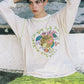 Person wearing a white t-shirt with colorful graphic design sitting on a wooden bench.