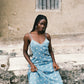 Woman wearing sheer blue sun embroidered slip with lace-trim neckline, spaghetti straps, and ethereal midi silhouette.