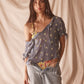 Woman wearing sheer blue blouse with delicate sunburst embroidery, drawstring neckline, and airy cropped silhouette for summer style.