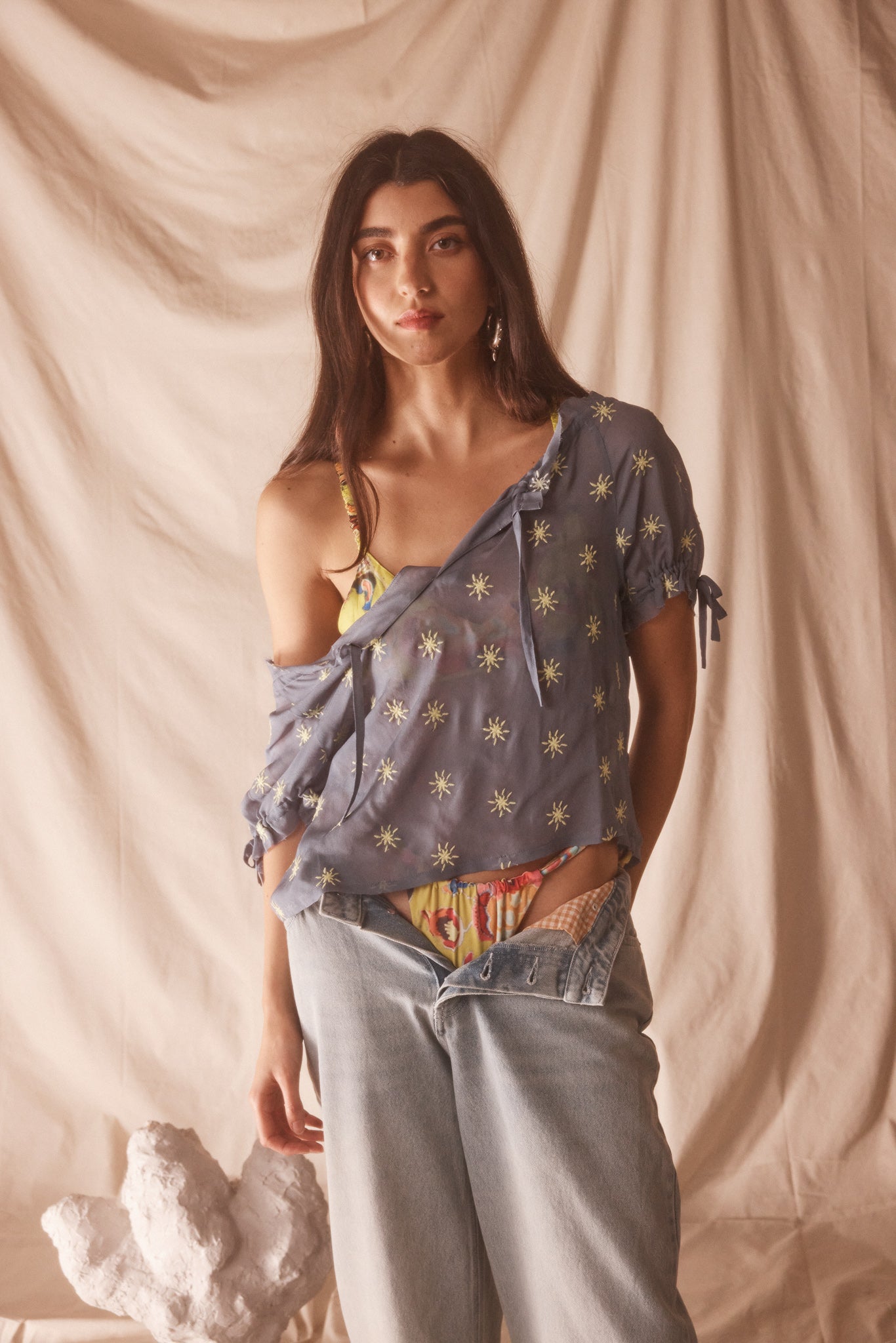Woman wearing sheer blue blouse with delicate sunburst embroidery, drawstring neckline, and airy cropped silhouette for summer style.