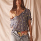 Woman wearing sheer blue blouse with delicate sunburst embroidery, drawstring neckline, and airy cropped silhouette for summer style.