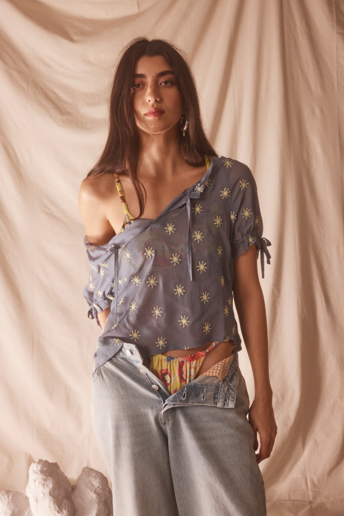 Woman wearing sheer blue blouse with delicate sunburst embroidery, drawstring neckline, and airy cropped silhouette for summer style.
