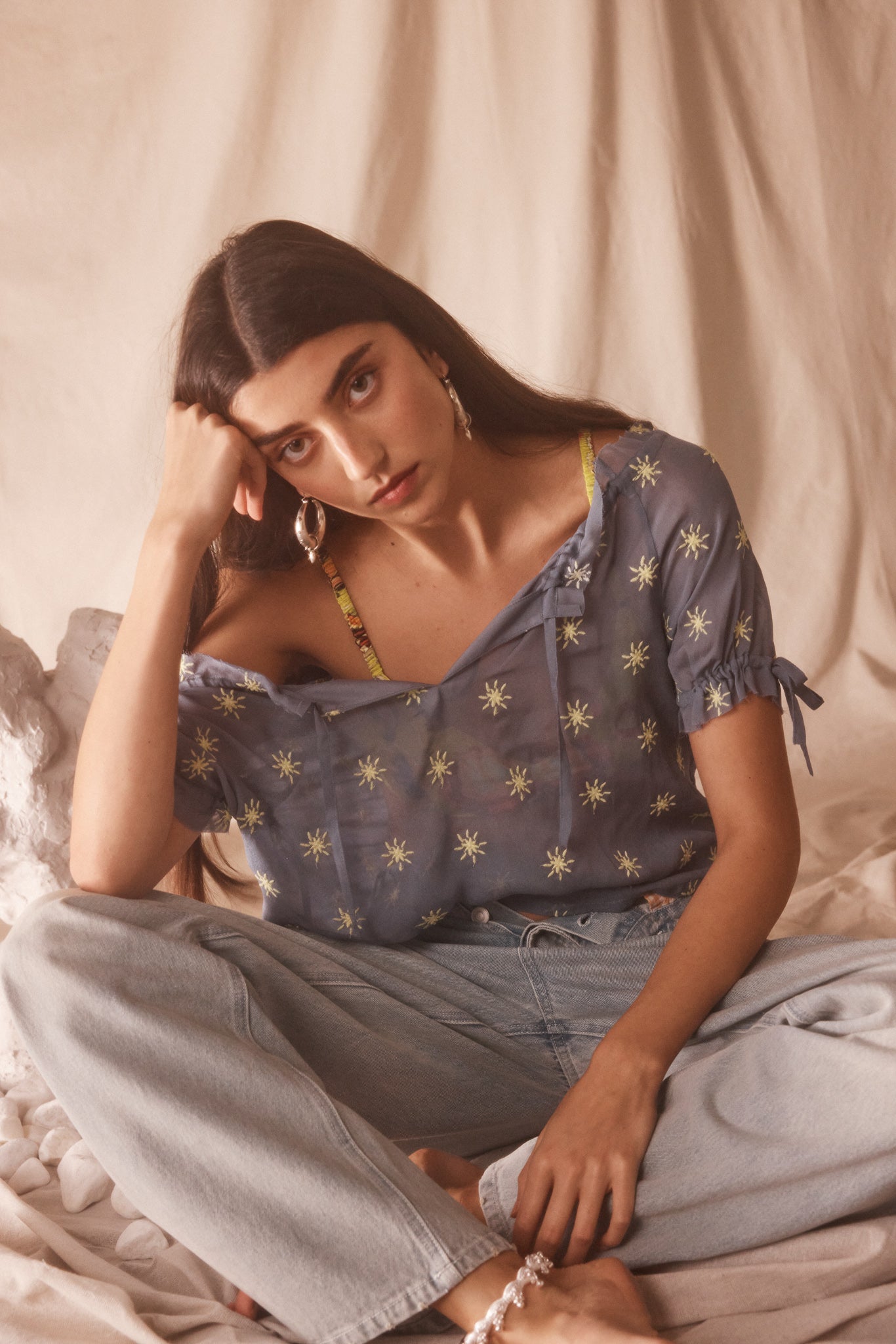 Woman wearing sheer blue blouse with delicate sunburst embroidery, drawstring neckline, and airy cropped silhouette for summer style.