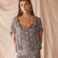 Woman wearing sheer blue blouse with delicate sunburst embroidery, drawstring neckline, and airy cropped silhouette for summer style.