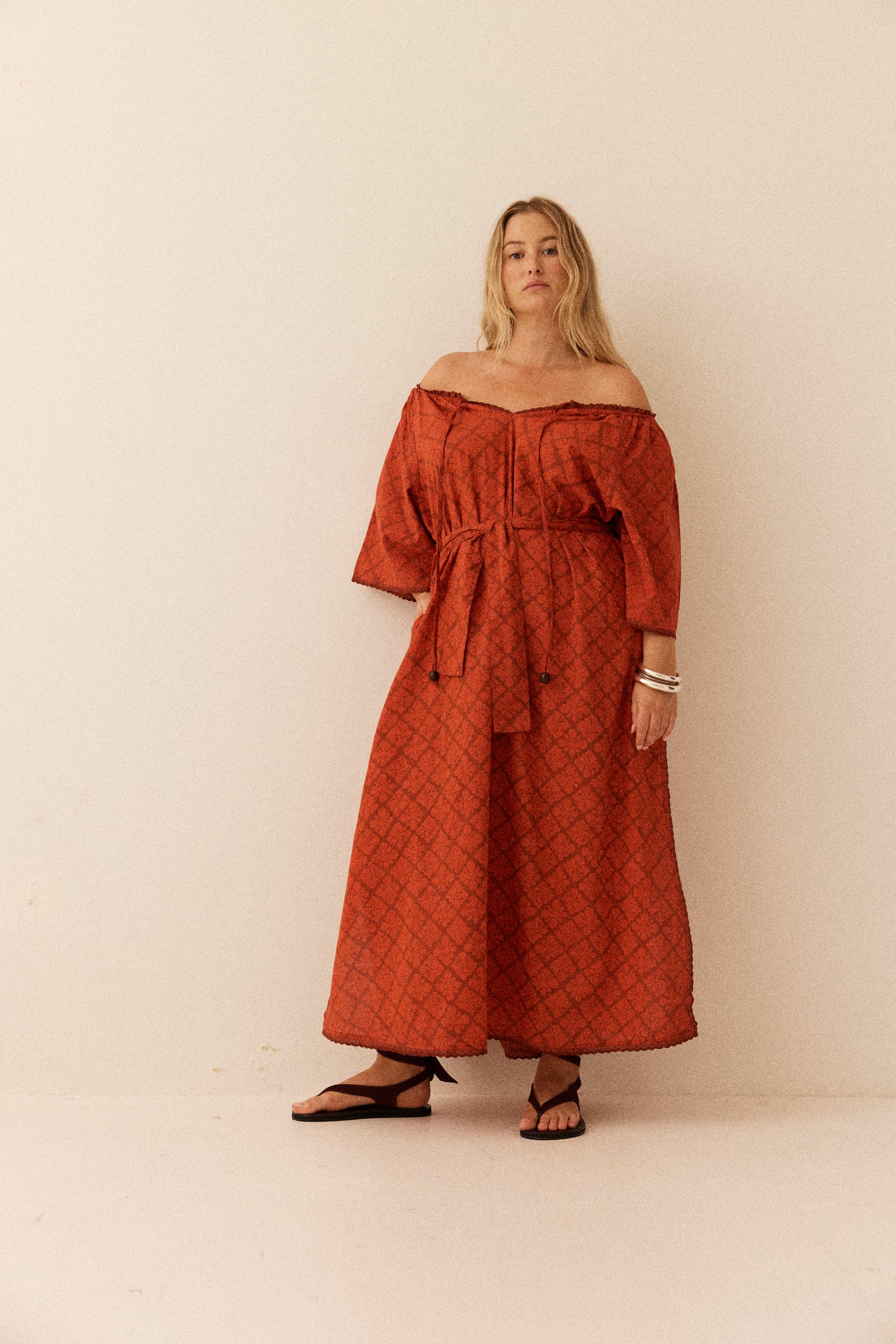 Woman wearing a rust-colored off-shoulder dress against a white background
