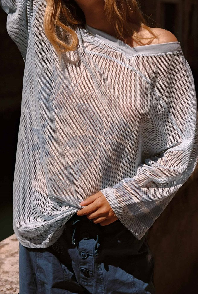 Close up of a woman standing in a light blue sheer oversized top with a palm tree graphic and the word 'KINGA' in blue.
