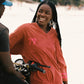 Woman in a red shirt dress standing next to a motorcycle on a beach.