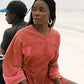Woman in a red and pink jersey with number 7 sitting on a beach.
