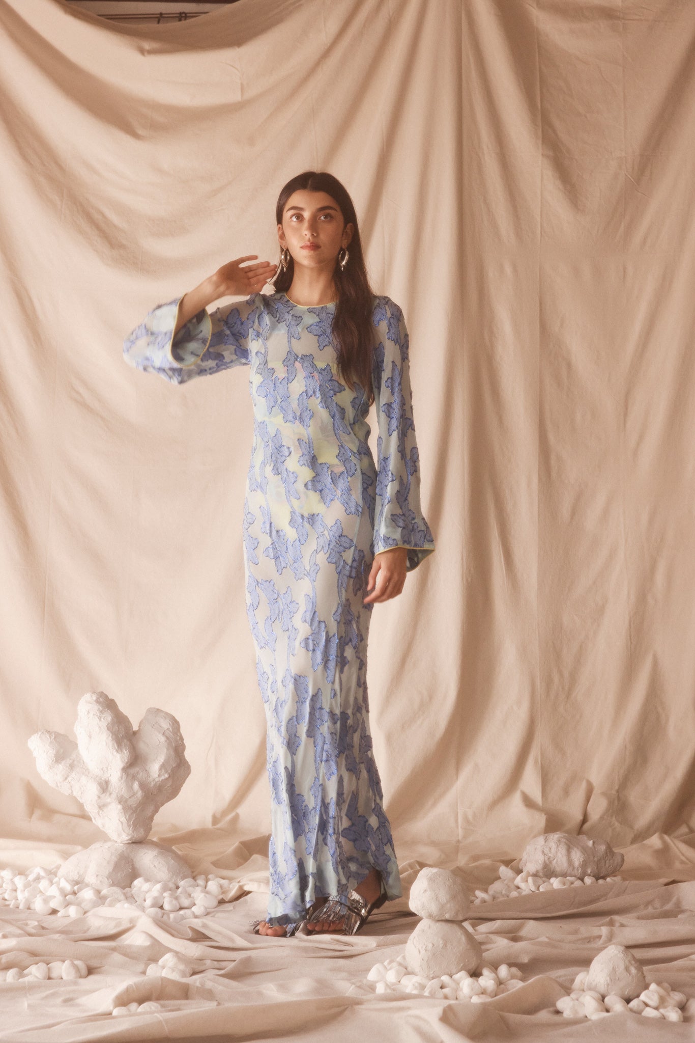 Woman wearing semi-sheer blue maxi with gold lurex florals, flared sleeves, and contrast piping. 