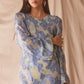 Woman wearing semi-sheer blue maxi with gold lurex florals, flared sleeves, and contrast piping. 