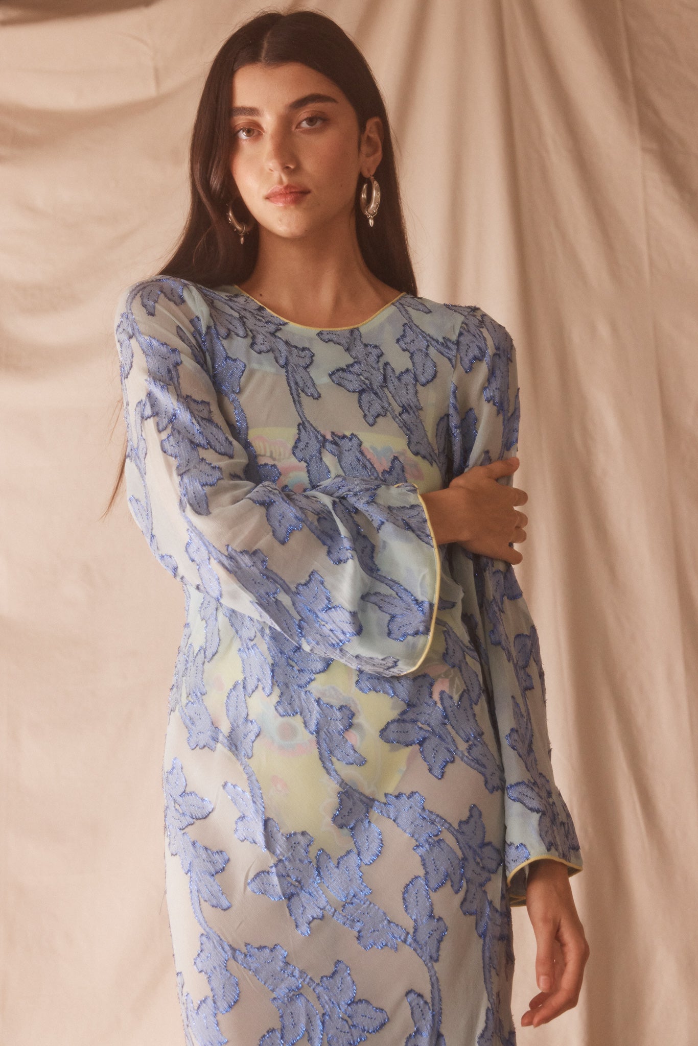 Woman wearing semi-sheer blue maxi with gold lurex florals, flared sleeves, and contrast piping. 