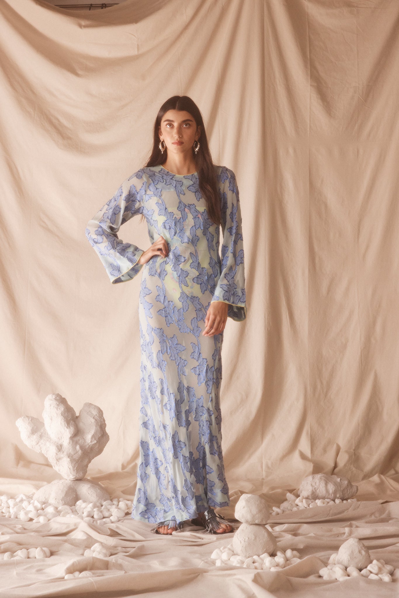 Woman wearing semi-sheer blue maxi with gold lurex florals, flared sleeves, and contrast piping. 