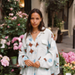 Model wearing Kinga Csilla Aquarius Chalm Shirt in baby blue linen with celestial brown and blue print, styled with matching Aquarius Column Skirt among pink flowers