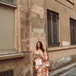 Model in Kinga Csilla Farfalla Jessi Pant and Farfalla Chalm Shirt, leaning against a Parisian stone wall while holding a city map, dressed in a bold orange butterfly print co-ord.