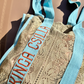 Kinga Csilla Rainy Lace KC Shoulder Bag in sage lace with aqua straps and orange logo embroidery, artisanal bohemian tote bag photographed in sunlight.