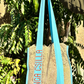 Kinga Csilla Rainy Lace KC Shoulder Bag held by model outdoors, featuring aqua blue straps, bold logo embroidery, and sage lace body design.