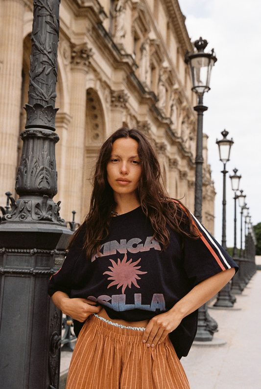 Model wearing Kinga Csilla Sunset Tee in black cotton with graphic sun print and striped sleeves, styled with Bello Swirl Jessi Pant  in a street-style setting
